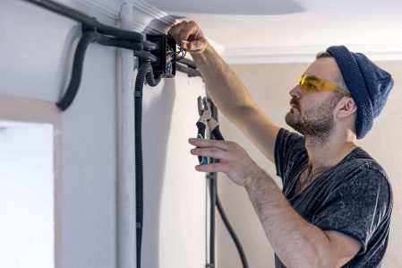 Attractive male electrician repairing an outlet, installing an outlet indoors.